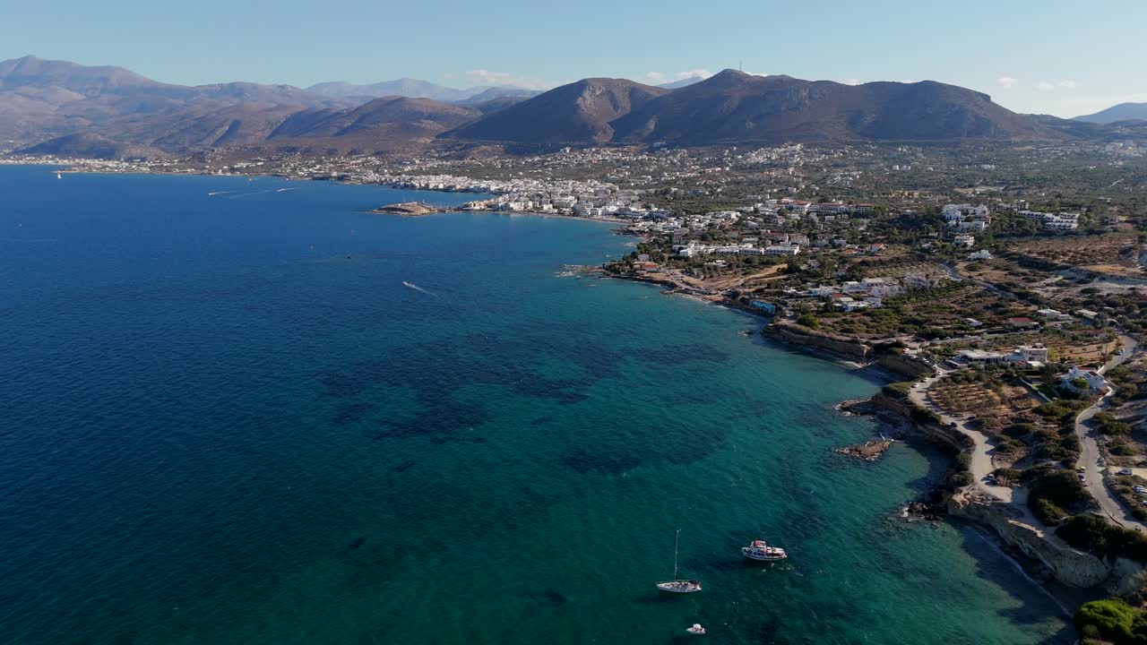 vista aérea de barcos atracados cerca de una costa turquesa con las montañas de creta en el fondo
