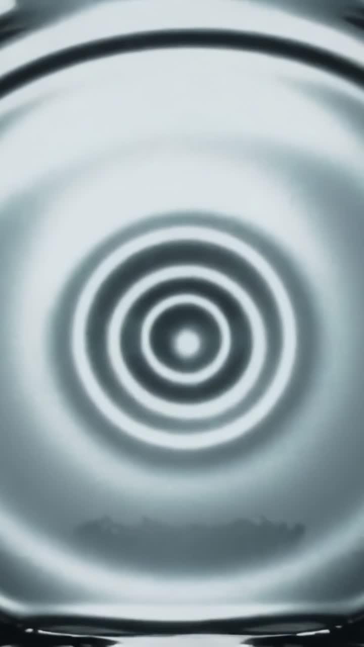 Vertical video: Central impulse starting expanding circular ripples in shallow basin, edges framing