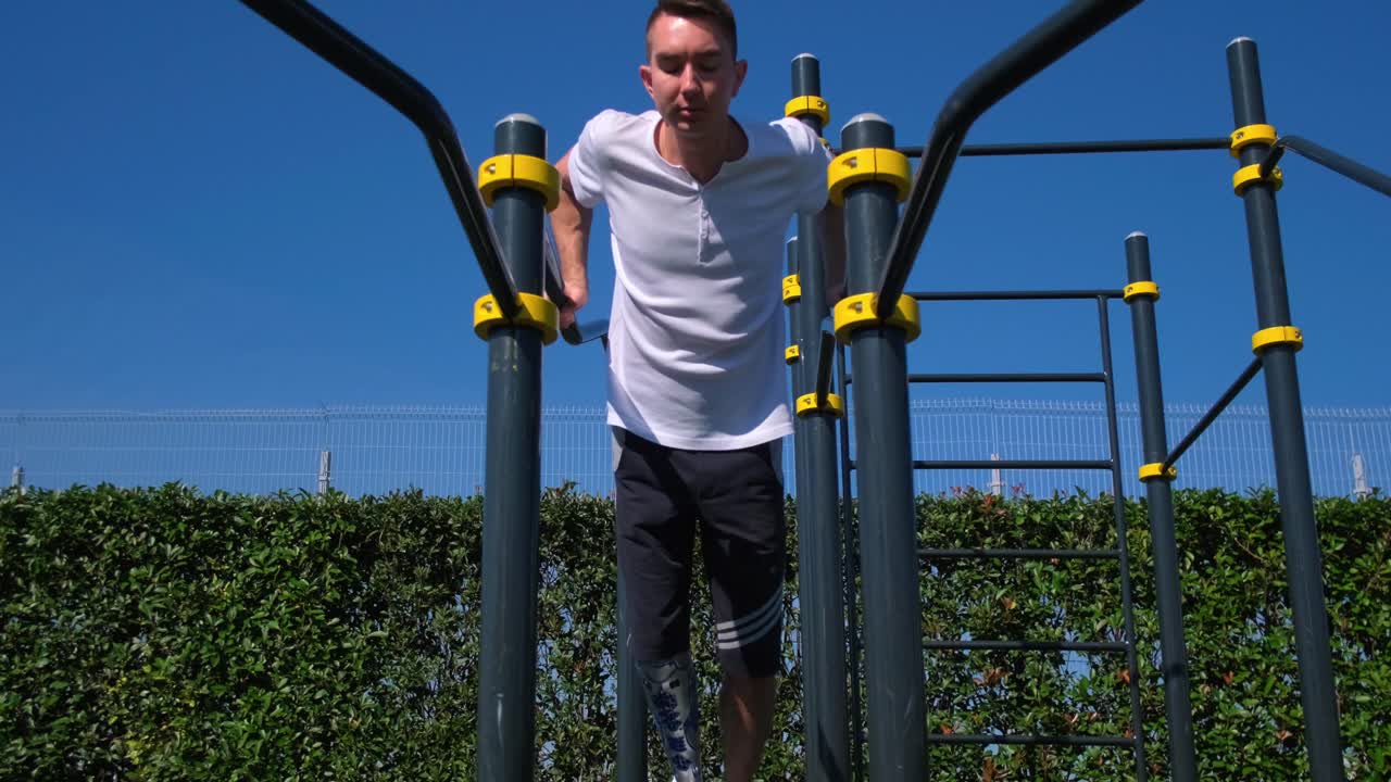 hombre con pierna protésica haciendo inmersiones en equipos de gimnasio al aire libre