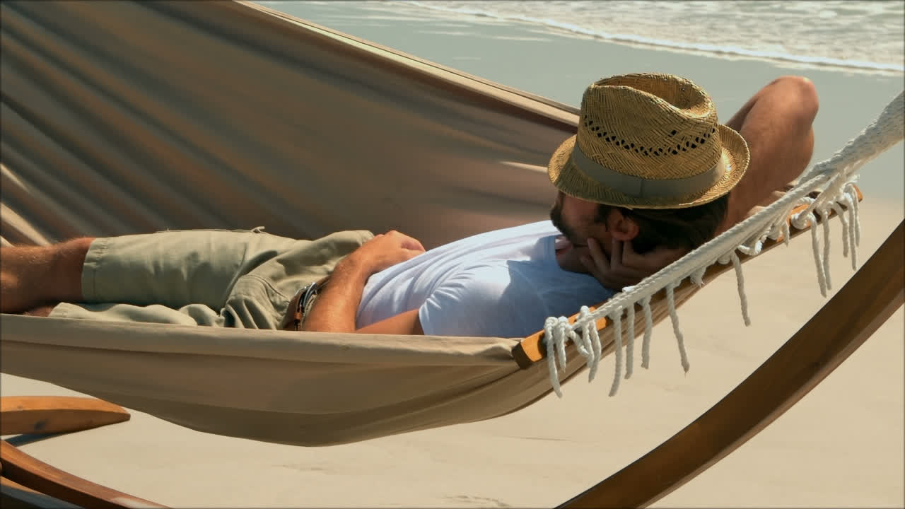 Side view of Caucasian man sleeping in a hammock on the beach 4k