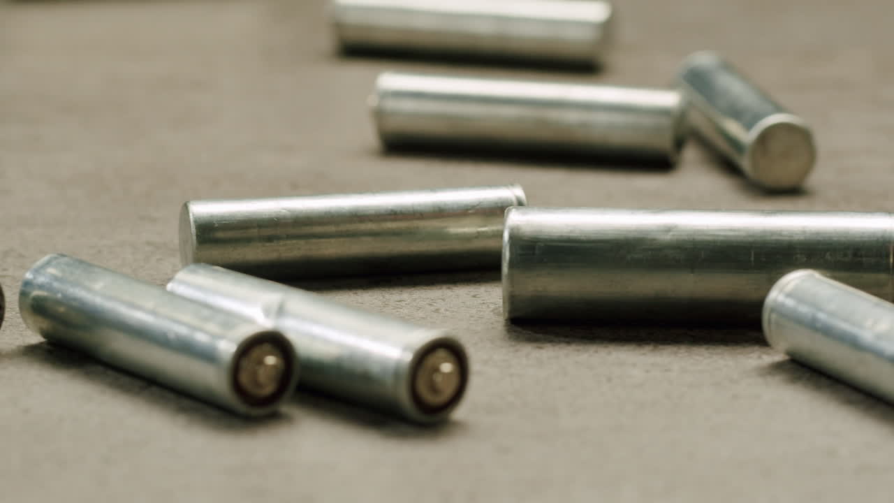 Silver batteries AA and AAA falling on grey table close-up. Double-A battery is a standard size single cell cylindrical dry battery. Batteries are common in portable electronic devices. Environmental impacts of lithium-ion batteries concept. An AA battery is composed of a single electrochemical cell