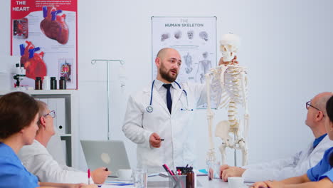 médico hombre apuntando a la columna cervical del esqueleto humano