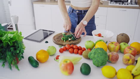 delicious fruit and vegetables on a table and woman cooking. housewife is cutting green cucumbers on a wooden board for making fresh salad in the kitchen. vertical video