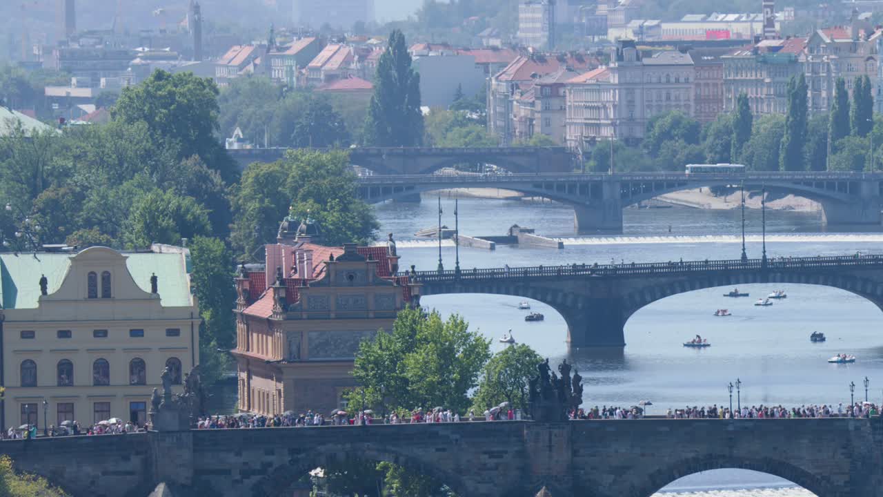 Folla di turisti e battelli fluviali si muovono sotto gli storici ponti nel panorama assolato di Praga, ampia ripresa aerea