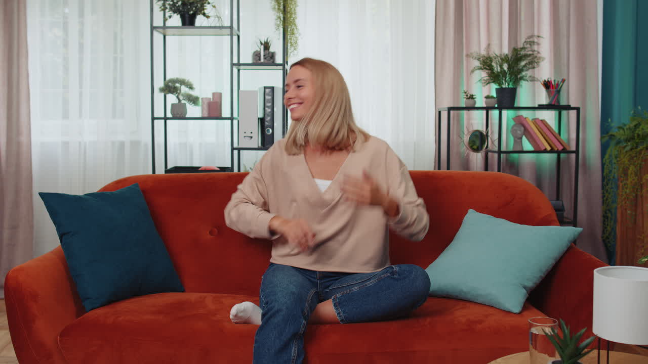 트렌디하고 즐거운 긍정적인 여성이 춤을 추고 리 ⁇ 에 따라 움직이며 현대 가정에서  ⁇  댄스 제스처를 만 ⁇ 니다.