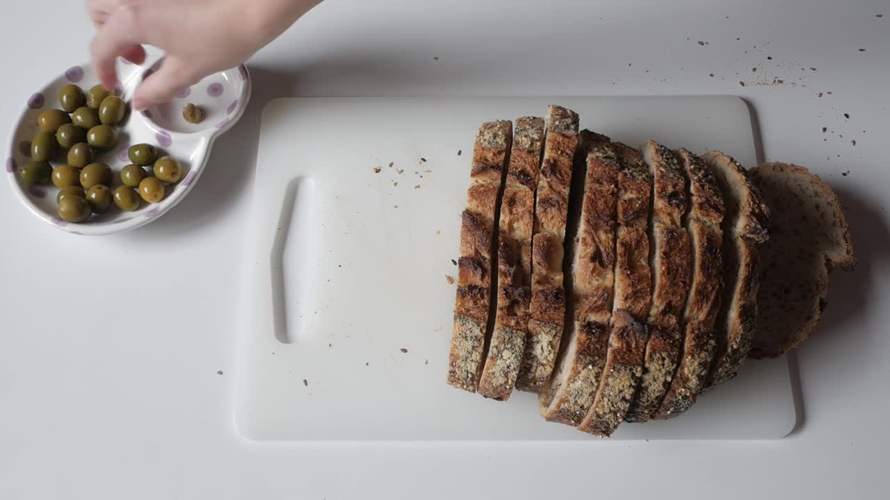 Pane alle olive appena affettato su un tagliere, accompagnato da olive verdi in una ciotola.