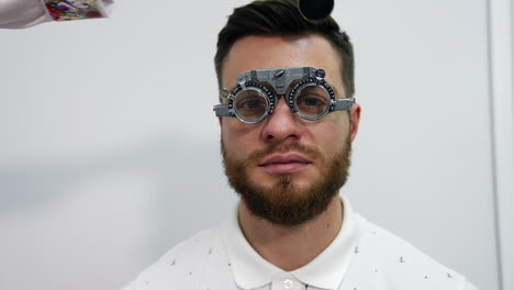 eyesight diagnosis in ophthalmology center. facial portrait of a young bearded man testing his eyes in trial frame. doctor checks patient's eyes in clinic.