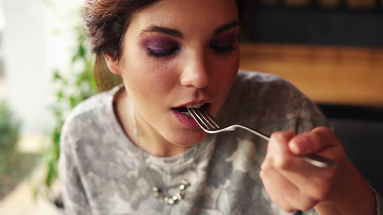 Camera movement from plate with rice and meat to woman's face. Close up of a young woman using fork to take fried meat with rice