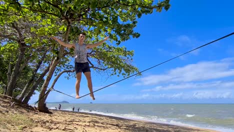 young adult male getting on slackline and balancing at trinity beach in cairns