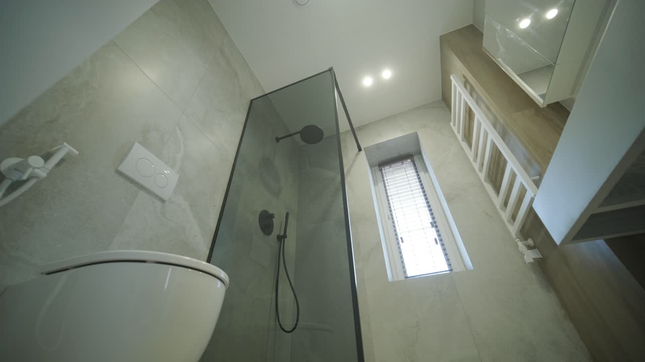 Un baño elegante y moderno con ducha con cerramiento de cristal, inodoro suspendido y elegantes azulejos de mármol