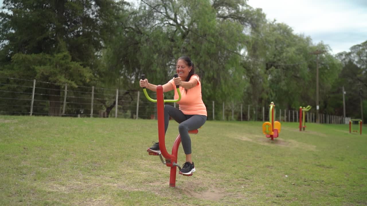 la mujer está utilizando un equipo de ejercicio de pedal en el parque - toma amplia