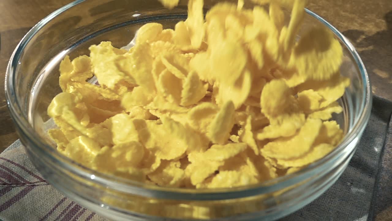 Knusprige gelbe Cornflakes in die Schale für ein köstliches Frühstück mit Milch am Morgen. Zeitlupe mit rotierender Kamerafahrt