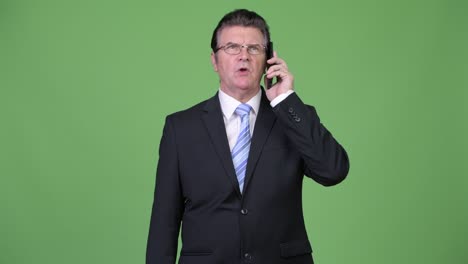 senior handsome businessman thinking while talking on phone
