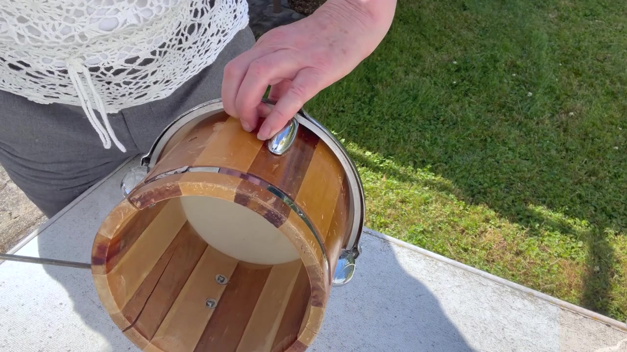 Un primo piano mostra un tamburo a mano tradizionale artigianale pulito con aria compressa. La polvere sottile si solleva. Scatto statico ravvicinato.