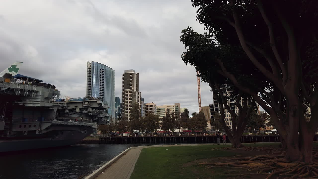 Wide shot of the USS Midway aircraft carrier docked along the Embarcadero with skyscrapers in the background