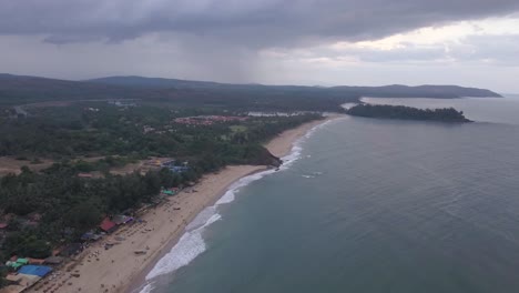 vista panorámica de la playa de arena con los turistas disfrutando en la playa de rajbagh, canacona, goa del sur, india - retirada aérea