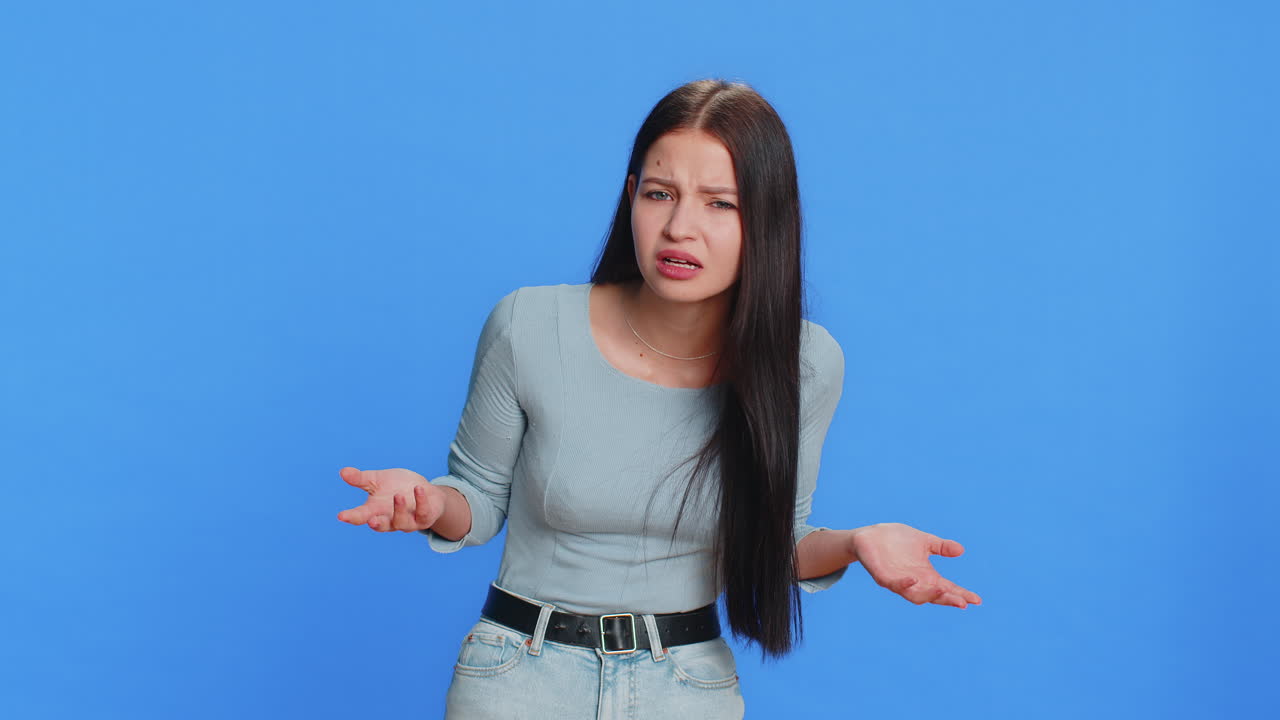 Young woman trying hear you looking confused and frowning keeping arm near ear for louder voice