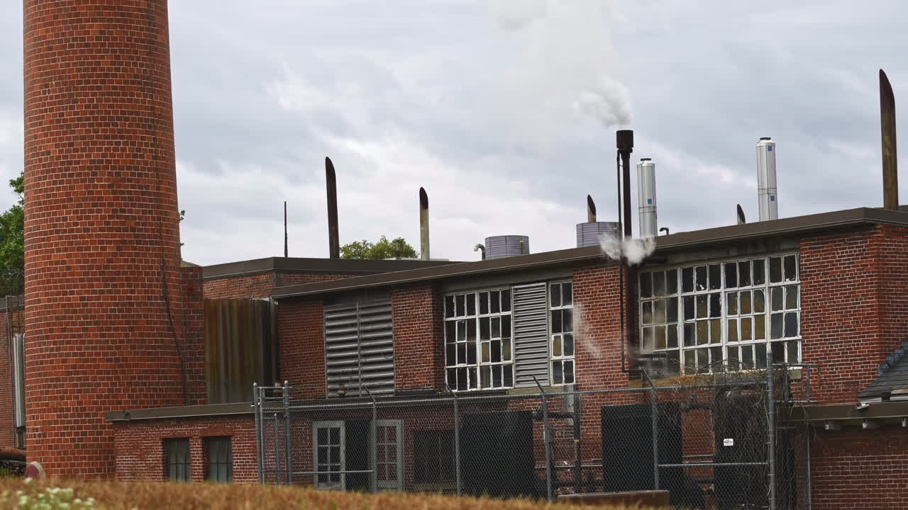 A red building with a chimney with cloudy sky. Bottom view of the building and the smoke