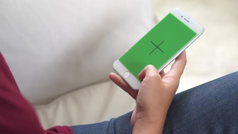 young asian woman using white smartphone device with green screen. asian woman mobile , scrolling pages while sitting on the couch in the living room. chroma key.