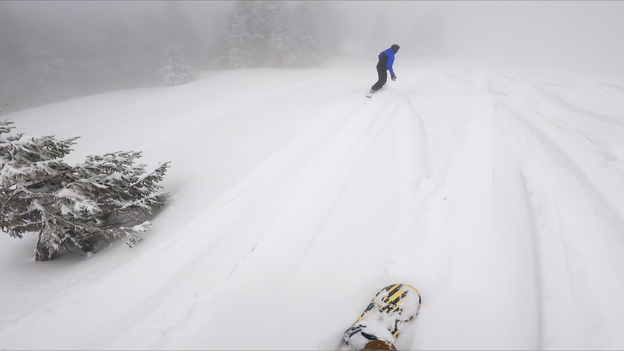 Going down the snowy slope of the mountain on the snowboard. Cameraman follows the snowboarder wearing blue and black sport suit.