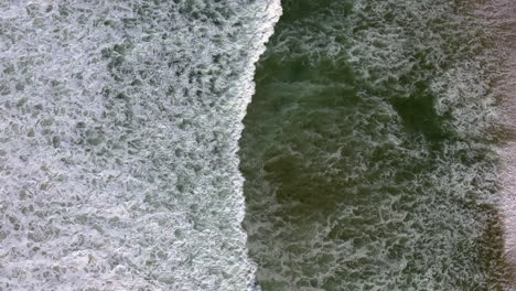 aerial drone view of ocean with waves crashing and sand shot in 4k high resolution