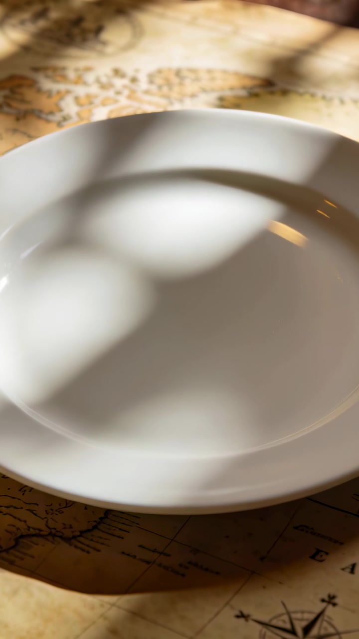 Il sole che si muove tra le piante, creando giochi di luce e ombre su un piatto bianco, una tovaglietta con mappa, annuncio di prodotto.