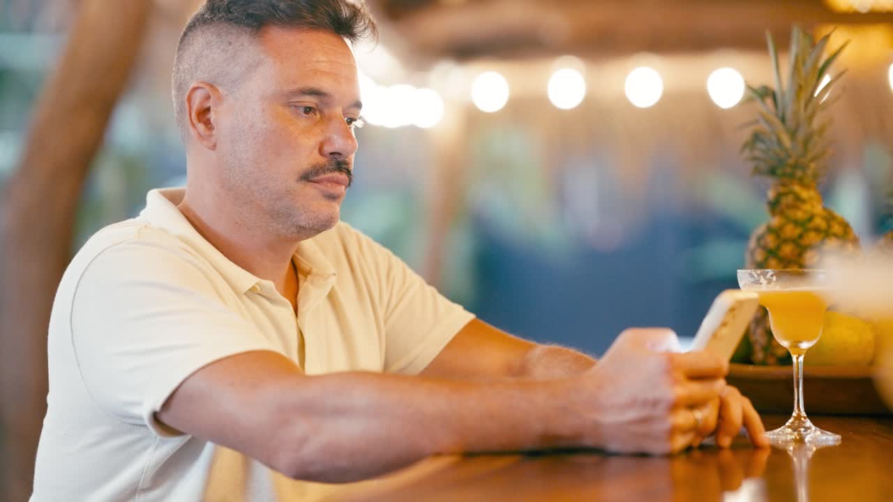 Man Looking at Smartphone While Sitting at a Tropical Bar