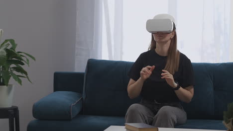 una mujer joven está usando una moderna pantalla hmd en la cabeza está sentada en la sala de estar moviendo las manos controlando por pantalla virtual tecnología moderna de realidad virtual