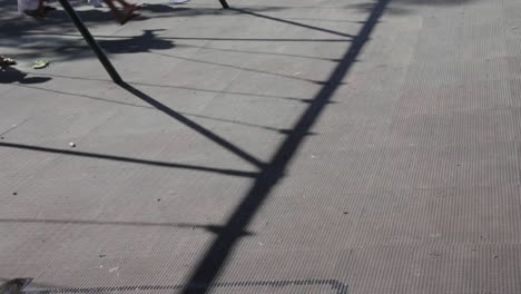 Kids-on-Swings-at-the-Park,-Shadows-Cast-on-the-Ground-from-Swing-Set,-Slow-Motion