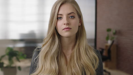 portrait of attractive young blonde woman executive boss looking serious at camera in office background