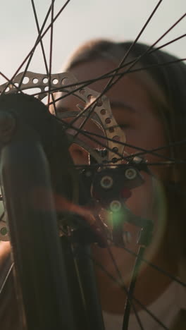 dama tocando suavemente la rueda de su bicicleta, sonriendo suavemente mientras la luz del sol se refleja en ella y la rueda giratoria, creando una atmósfera serena, con un fondo borroso de exuberante vegetación