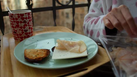 Woman-in-Pajamas-Prepares-and-Enjoys-Turkey-Slices-with-Bread-and-Cheese-on-Cozy-Balcony-hands-detail-shot