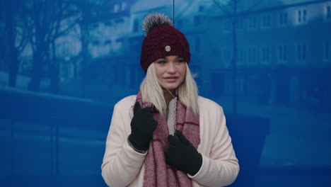 atractiva mujer caucásica vestida de invierno apoyada en una pared de cristal azul con reflejo de estructura