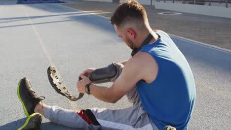 atleta masculino caucásico discapacitado sentado, poniéndose la cuchilla para correr