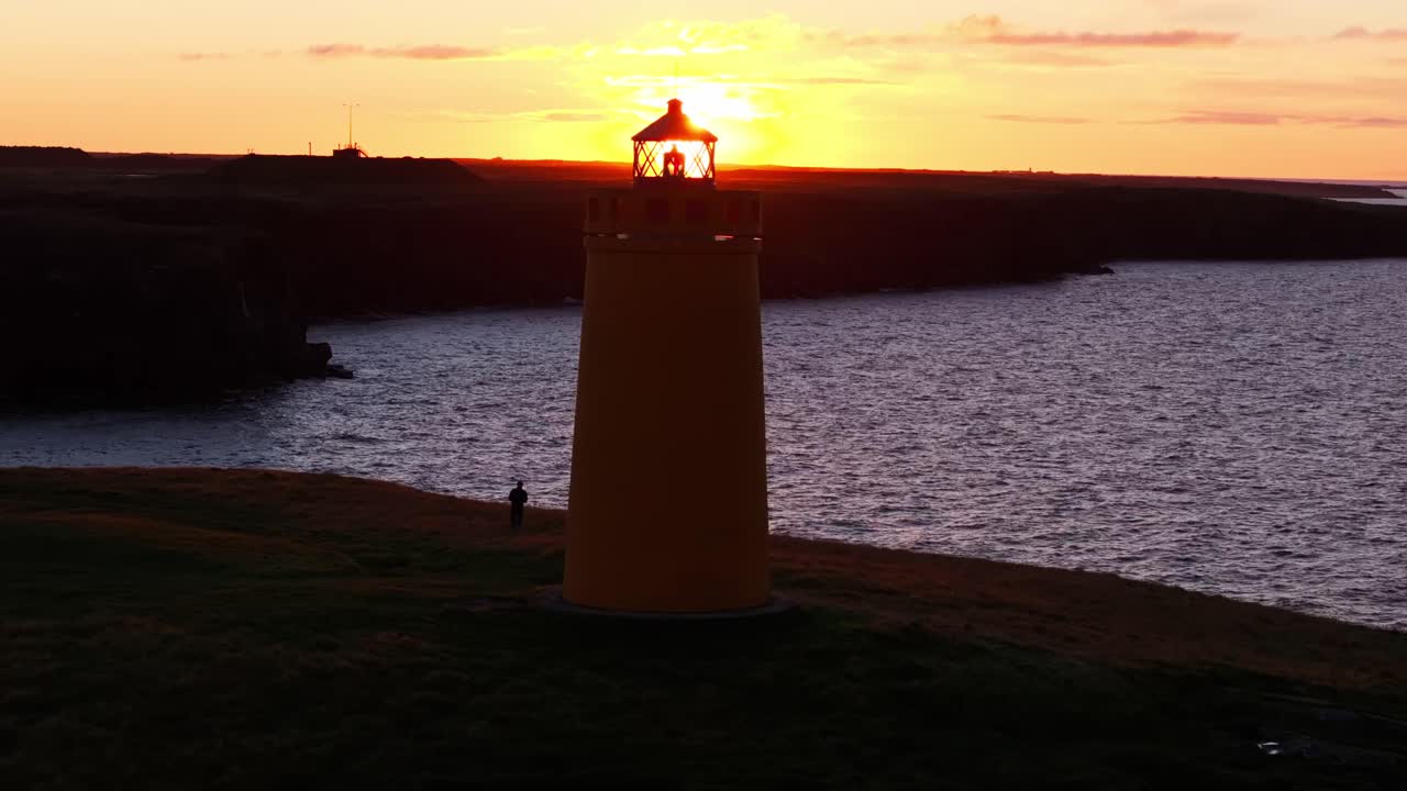 Uomo a passeggio al Faro Giallo di Keflavik, vicino alle scogliere oceaniche, in un drammatico paesaggio islandese.