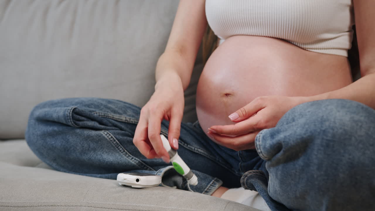 Pregnant woman sits on couch holding fetal doppler device to monitor babys heartbeat during