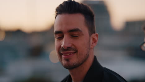retrato atractivo joven hombre caucásico en el techo al atardecer sonriendo feliz disfrutando de la vida nocturna urbana con luces de la ciudad bokeh en el fondo