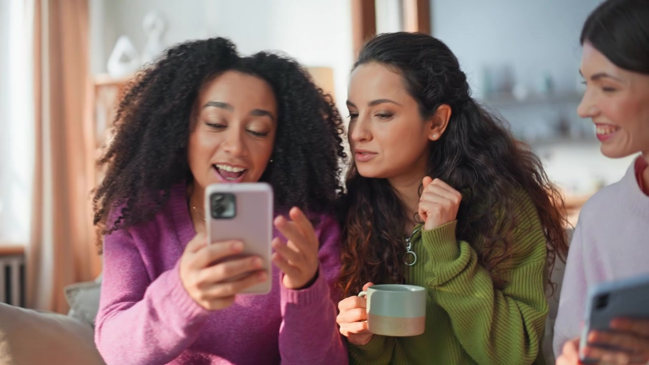 Relaxed women looking mobile phones sitting couch closeup. Multicultural friends