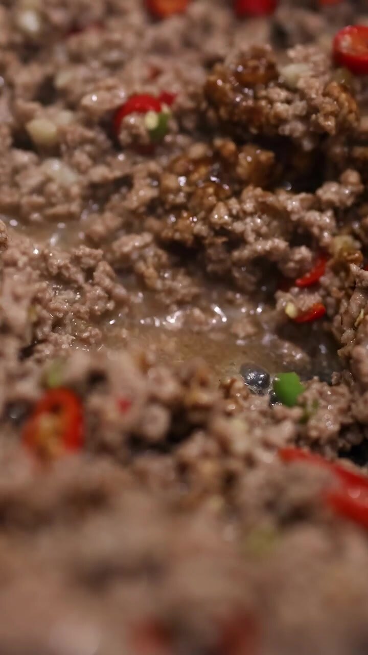 Close-up tumis daging sapi yang sedang dimasak dengan paprika merah dan hijau. Pencahayaan hangat, sudut kamera dinamis, dan suasana mendesis.