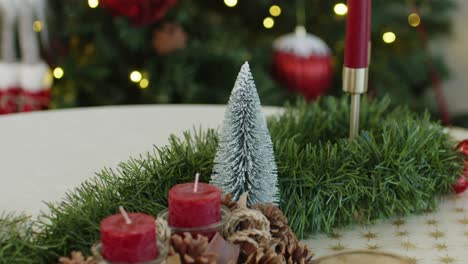 christmas pine centerpiece with red candles and snowy fir tree on decorated table