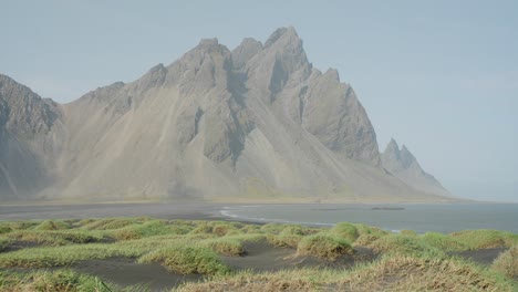 una impresionante vista del monte vestrahorn en el borde de un océano con una pradera azotada por el viento en primer plano