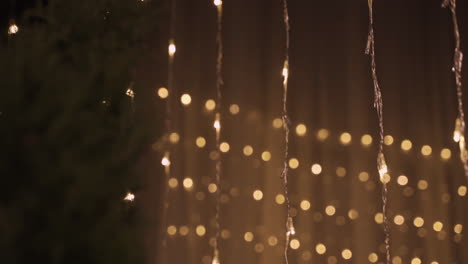 camera focuses on garlands of golden christmas lights in dark party room decorated with christmas tree 2