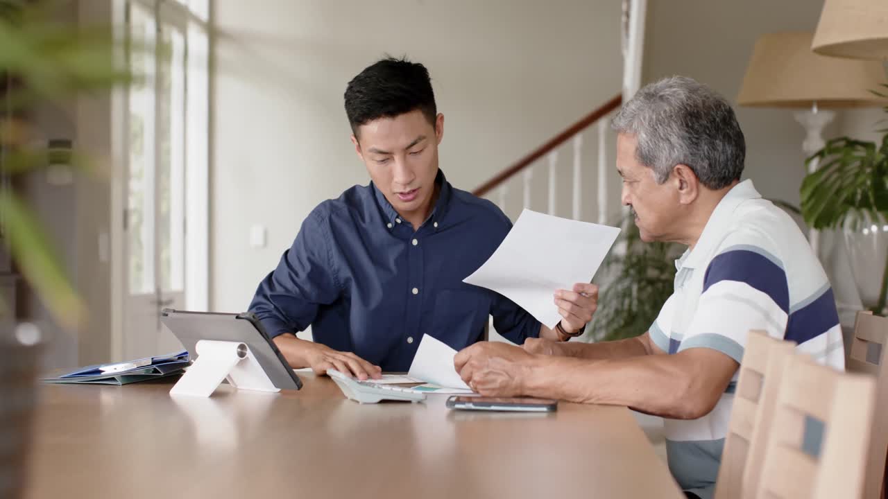 Happy diverse financial advisor and senior man discussing paperwork and using tablet at home
