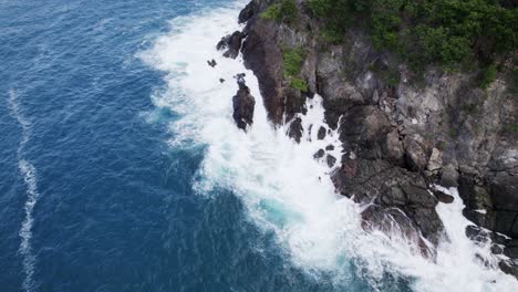 Beautiful-aerial-wide-shot-of-water-crashing-on-rocks-below-cliffon-the-beach-shore-sand-turquoise-water-relaxation-vacation-tourism