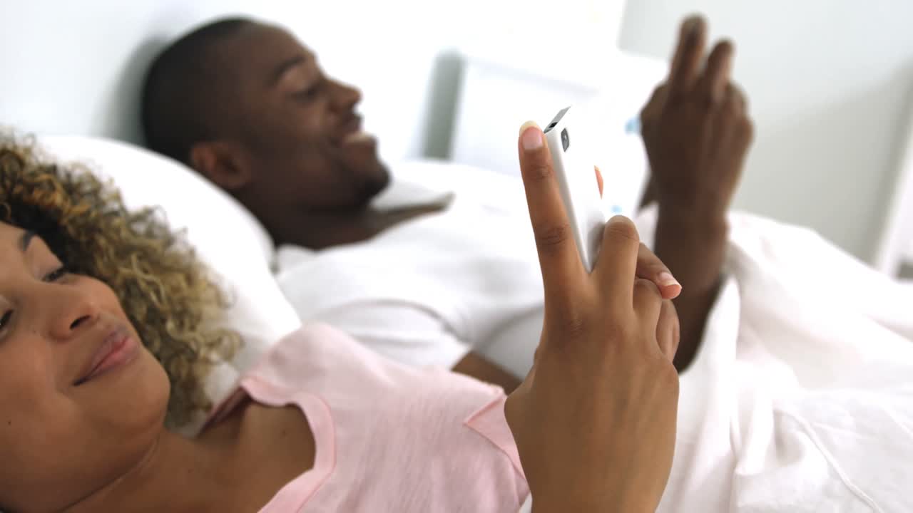 Happy couple using mobile phone on bed