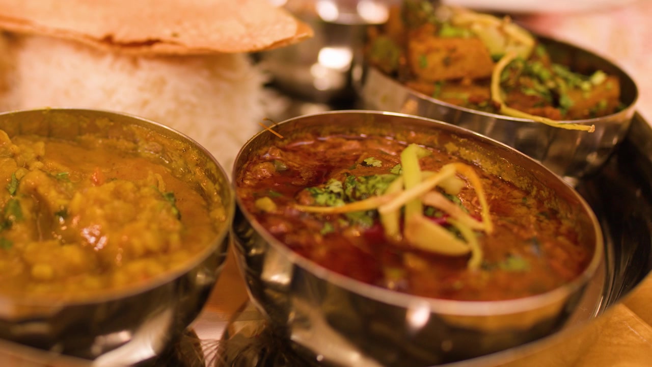Primer plano de un tenedor sumergiéndose en curry dal sobre una bandeja thali de metal.