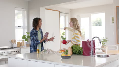 una pareja feliz y diversa desempaquetando bolsas de compras en la cocina, en cámara lenta.