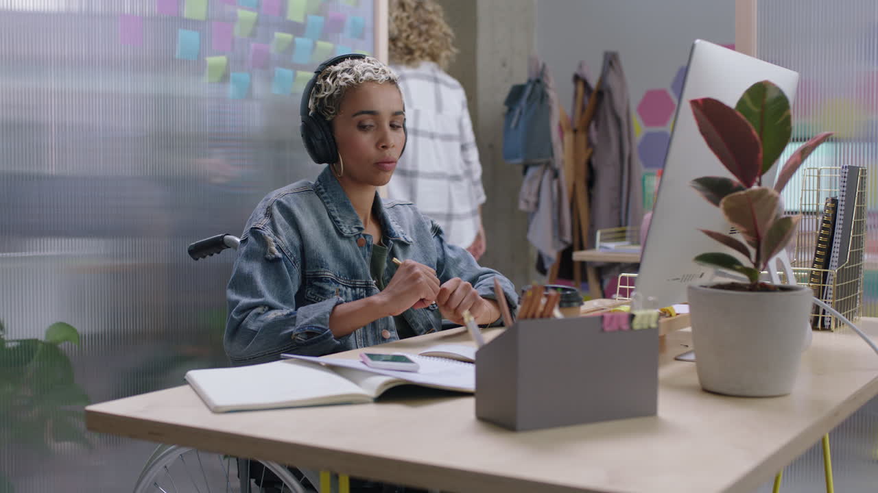 young disabled african american business woman using computer brainstorming browsing online research ideas for startup company listening to music wearing headphones in modern office