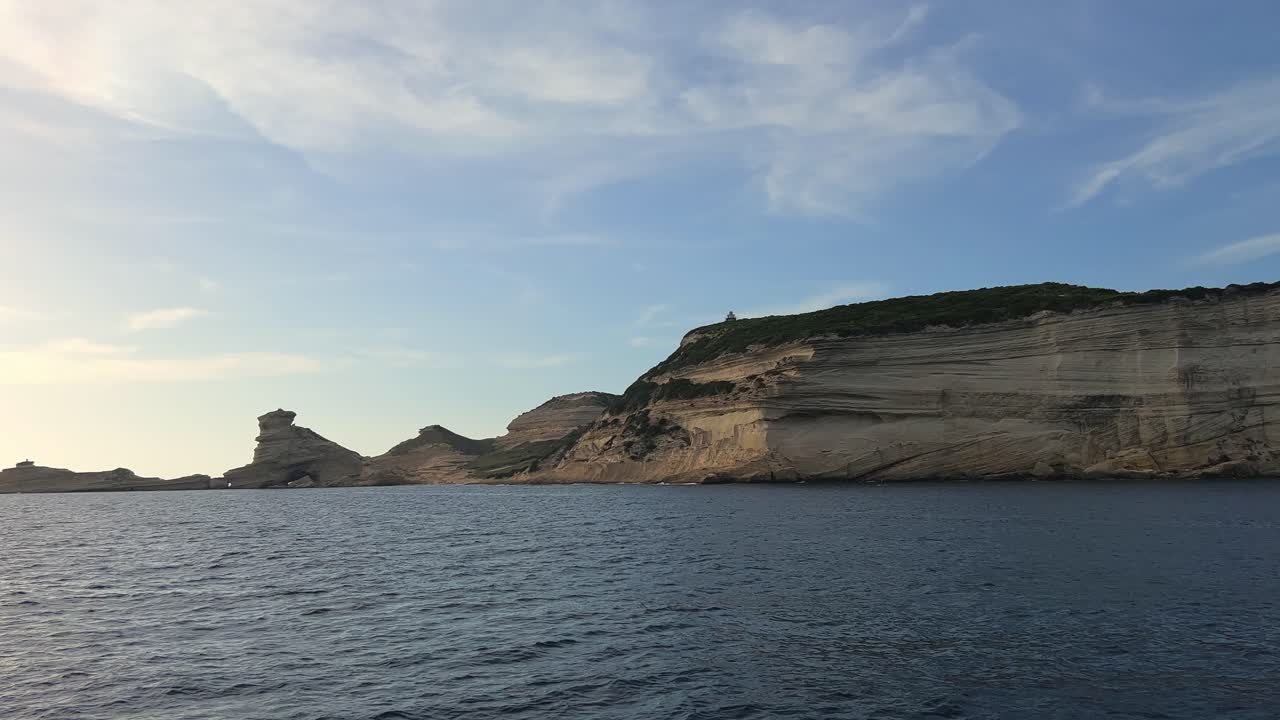 Pov of sailboat bow navigating toward Corsica island cliffs and Capo Pertusato lighthouse in France, 50fps