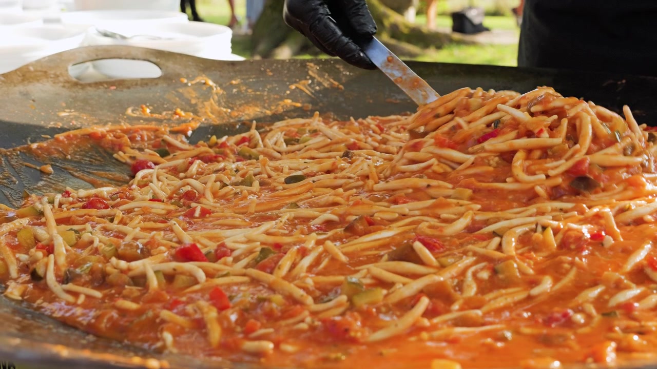 Cucina di cibo tradizionale locale con sugo di verdure per la pasta. Uno chef prepara e mescola in una grande padella all'aperto in una giornata di sole
